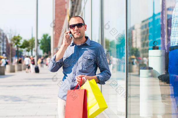 年轻人手里拿着许多彩色购物袋在<strong>商场</strong>购物。他拿着一部电话。