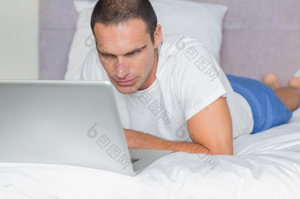 专心的男人躺在床上用笔记本电脑