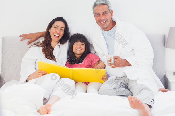 父母和女儿躺在床上一起看相册