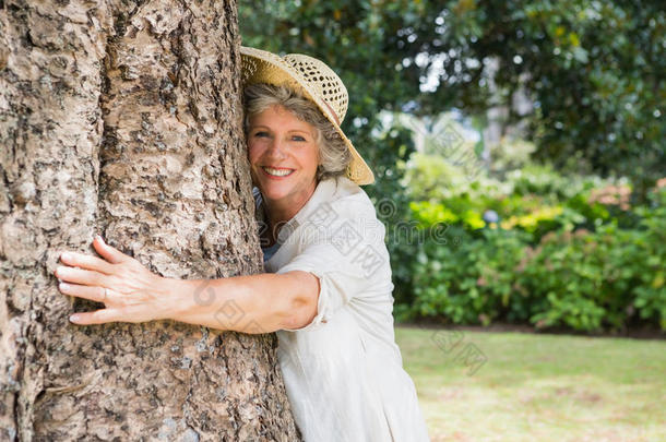 一位退休妇女抱着一棵树对着镜头微笑