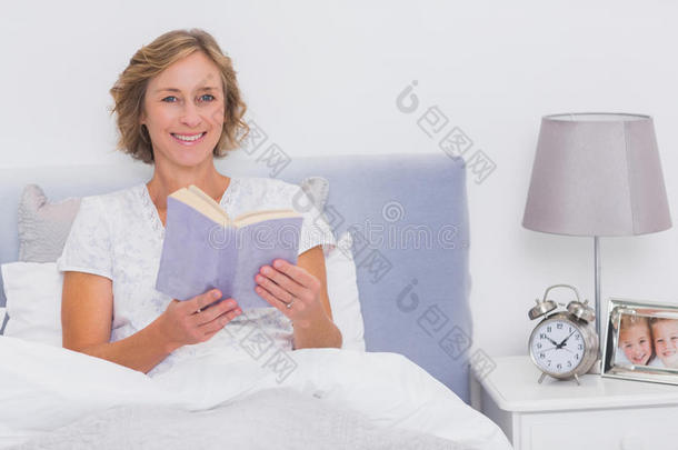 放松的金发女人坐在<strong>床</strong>上拿着书