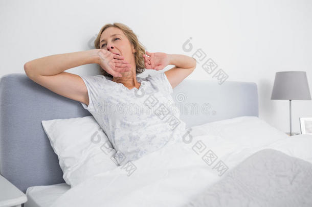 一个金发女人早上在床上打哈欠、伸懒腰
