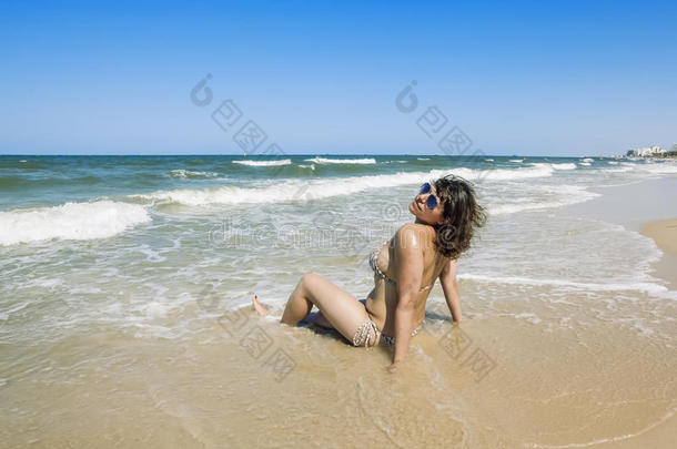 穿着比基尼晒得黝黑的女孩在海滩上的海浪中尽情挥洒