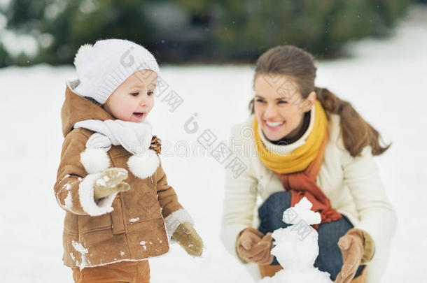 快乐的妈妈和宝宝在冬季公园堆雪人