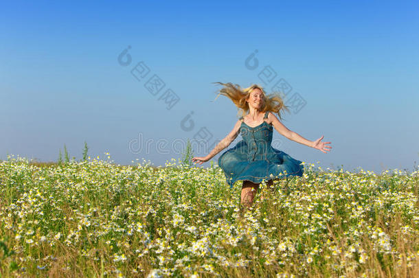一位身穿蓝色太阳裙、长着一头金发的妇女，在蓝天映衬下，在甘菊的田野里欢快地移动着