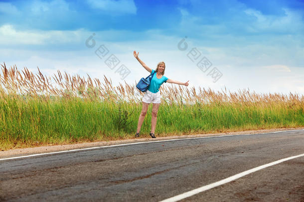 那个苗条的女孩，一头金色长发，穿着蓝色t恤和白色短裤，在通往阳光明媚的<strong>夏日</strong>的路上拦住了一辆经过的<strong>汽车</strong>