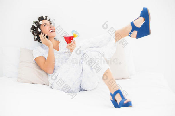 穿着卷发鞋和楔形鞋的黑发女人，拿着鸡尾酒在床上叫唤