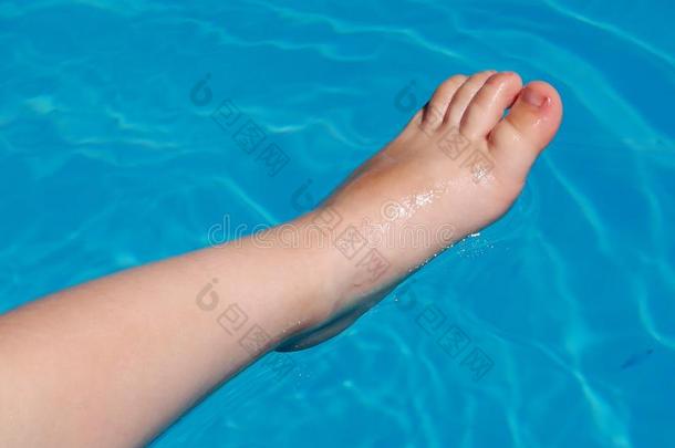 半脚浸在蓝色游泳池水中的儿童腿