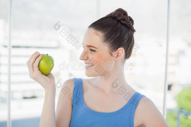 手持青苹果、身穿运动服、面带微笑的苗条女子