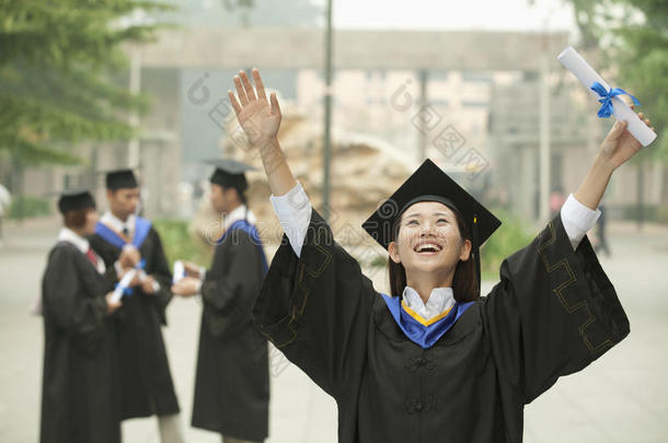 年轻的女<strong>大学毕业</strong>生，举起手臂举着文凭