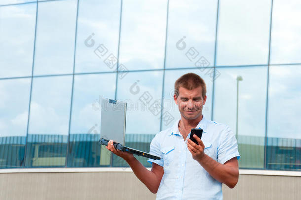 现代商务楼前手持手提电脑和手机的男子