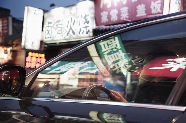 年轻人晚上开车穿过<strong>北京</strong>，车窗上反射出商<strong>店</strong>的灯光