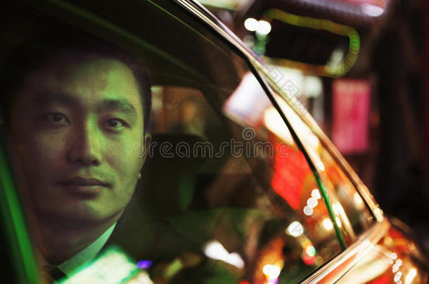 北京，一位沉思的商人坐在一辆汽车的后座上，夜晚透过车窗向外望去