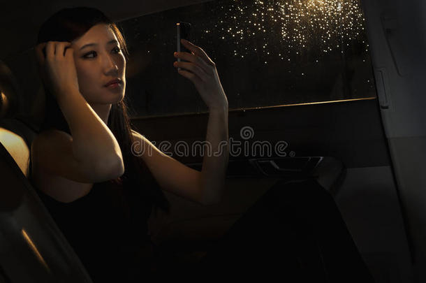 北京一个雨夜出门前，一位年轻女子坐在车里用电话检查头发