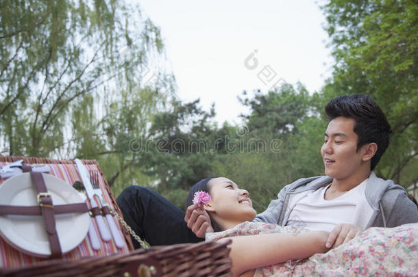 一对微笑的情侣在公园里野餐，躺在毯子上，野餐篮打开