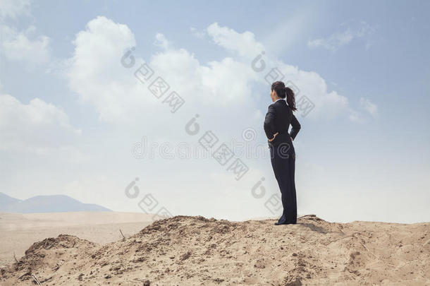 年轻的女商人双手叉腰站在沙漠上空
