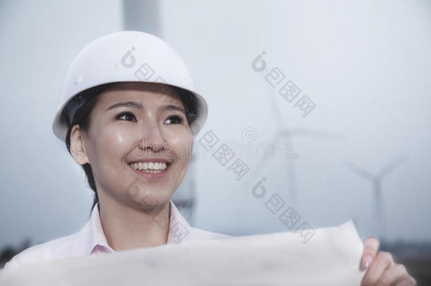 年轻微笑的女工程师拿着一张有风力涡轮机的蓝图