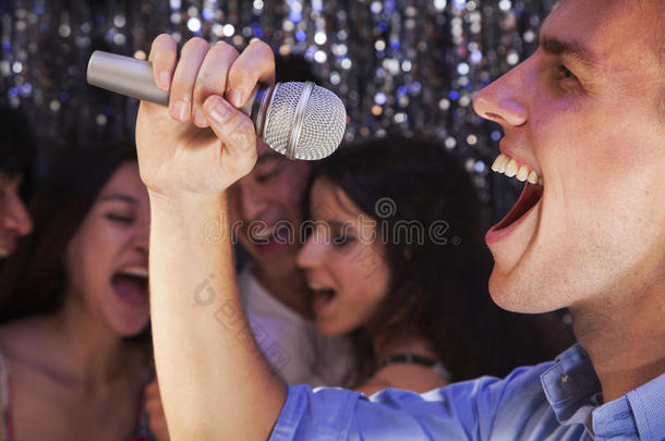 特写镜头：年轻人拿着麦克风在卡拉OK唱歌，朋友们在后台唱歌