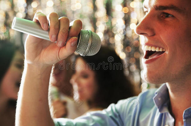 特写镜头：年轻人拿着麦克风在卡拉OK<strong>唱歌</strong>，朋友们在后台<strong>唱歌</strong>