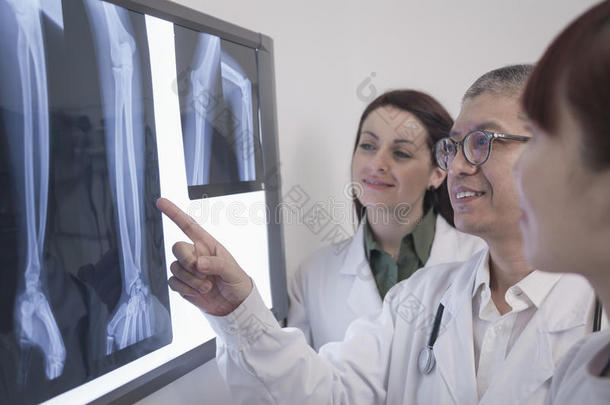 三个面带微笑的医生看着人体骨骼的x光片，一个医生指着