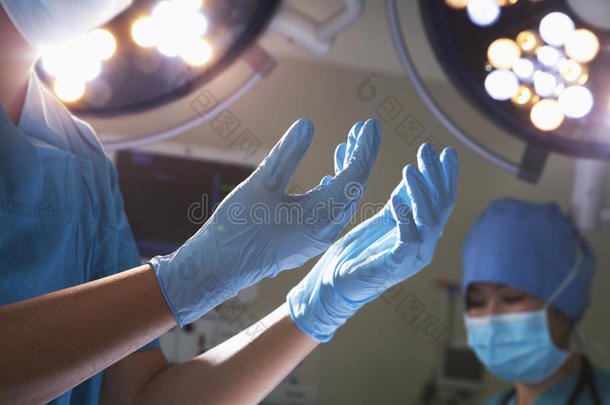 手术室戴手术手套和手术灯的双手正中视图