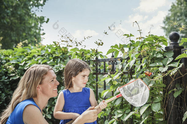带着微笑的母女抱着一只蝴蝶，试图在花园里捉一只蝴蝶