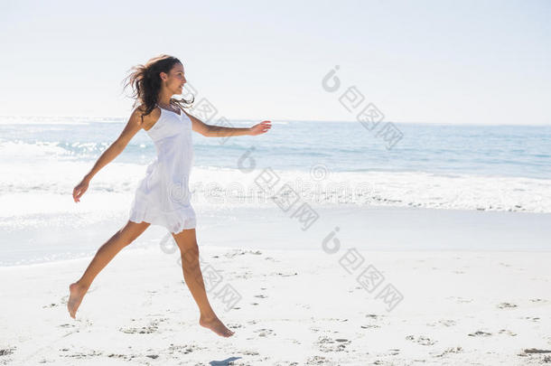 快乐的黑发<strong>女郎</strong>穿着白色太阳裙在<strong>沙滩</strong>上蹦蹦跳跳