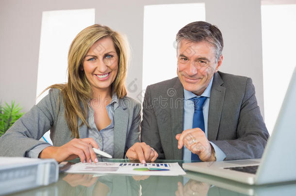 两个高兴的商人对着镜头微笑着分析一张图片