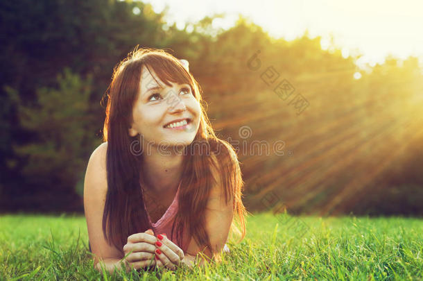 年轻漂亮的女人躺在草地上，在<strong>夏日</strong>的<strong>夕阳</strong>下微笑