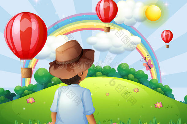 山顶上一个男孩，带着飞扬的气球和彩虹