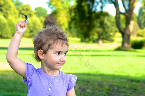 小女孩，小女孩，蹒跚学步的孩子，在公园里玩耍时<strong>高举</strong>着一根羽毛。