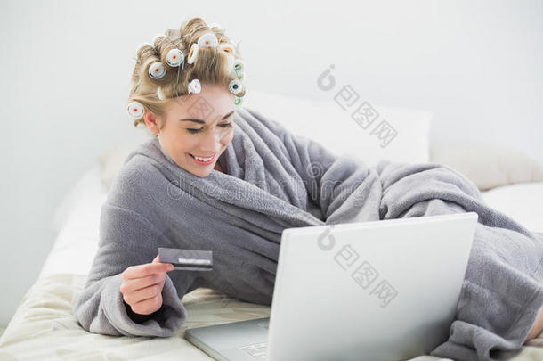 一位穿着卷发器、心情轻松的金发<strong>女士</strong>在网上<strong>用笔记本电脑</strong>购物