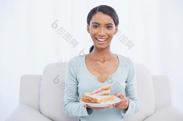 微笑迷人的女人坐在舒适的沙发上拿着三明治