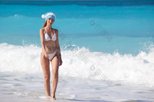 戴着新年帽的年轻女子在阳光明媚的日子里走在海滩上