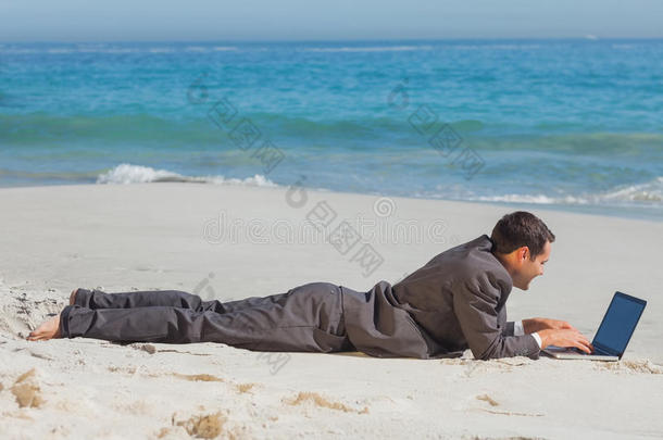 躺在沙滩<strong>上</strong>用笔记本打字的年轻商人