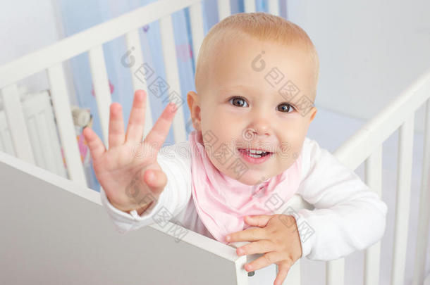 一个可爱的婴儿在婴儿床上挥手打招呼并微笑的画像