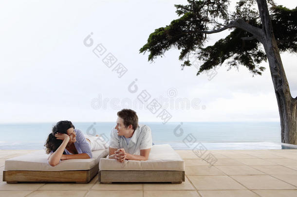 幸福夫妻在无限泳池边的日光浴床上放松