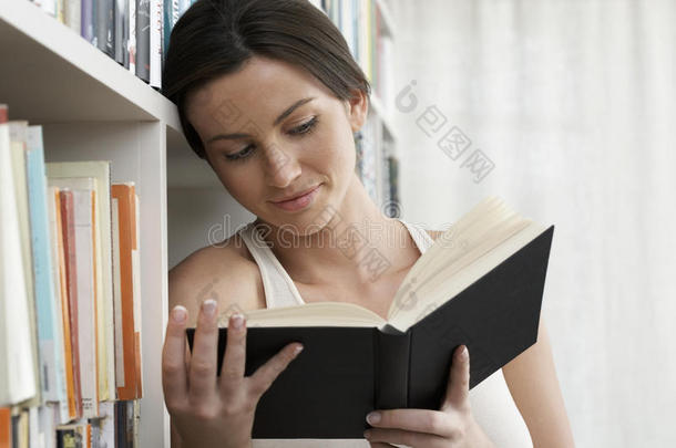 在家里靠书架看书的女人