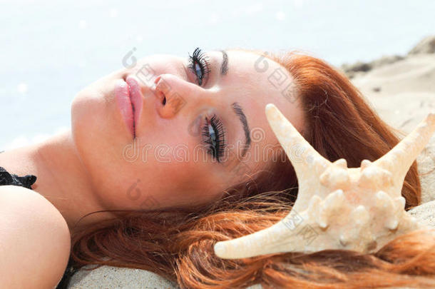 美丽的女孩躺在海边，带着贝壳自然度假