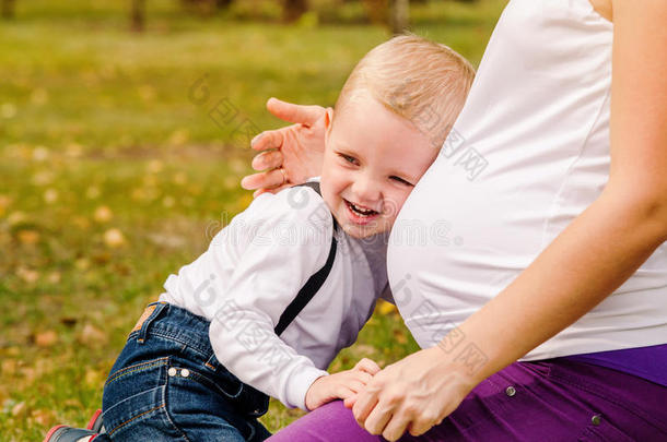 快乐微笑的孩子靠近怀孕的妈妈肚子