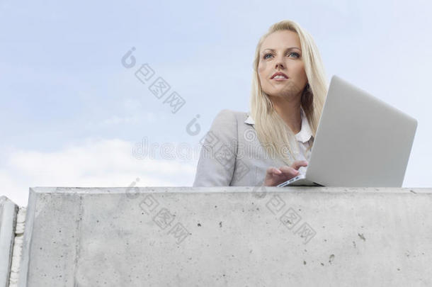 拿着笔记本电脑的年轻女商人仰望着天边的露台
