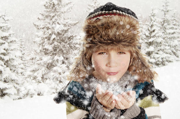 快乐的男孩在冬天的风景里吹雪花