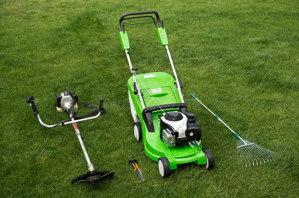 草坪上的绿色割草机、除草机、耙子和割草机