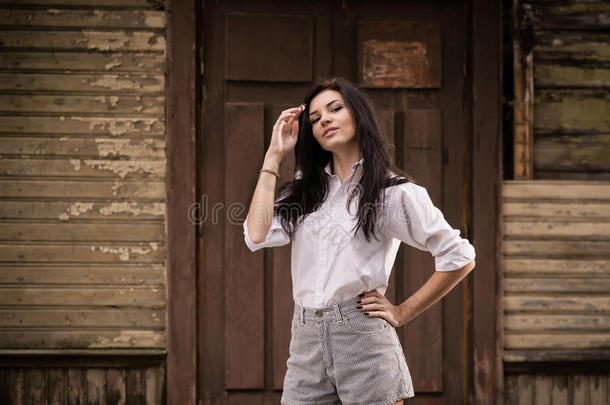一位时尚<strong>靓丽</strong>的年轻女子在户外靠近一堵旧木墙摆姿势