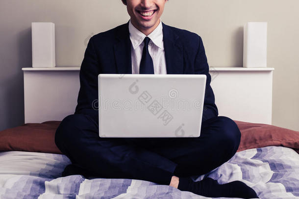 快乐的年轻商人坐在床上拿着笔记本电脑