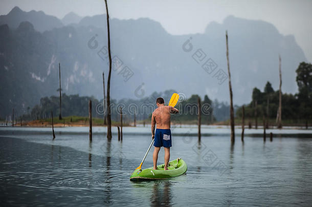 在泰国风景如画的湖面上划独木舟的强壮的年轻人。