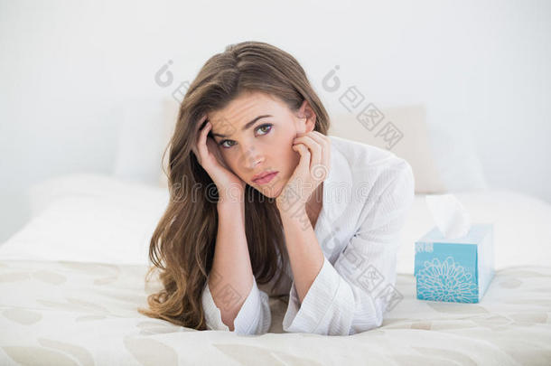 沮丧的棕色头发的女人穿着白色睡衣躺在床上