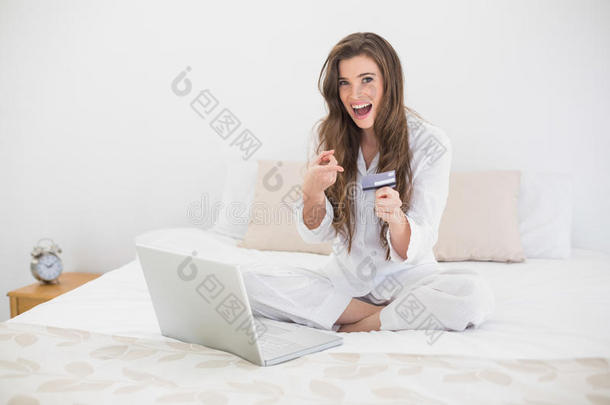 一位穿着白色睡衣的棕色头发的女士用笔记本电脑在网上购物
