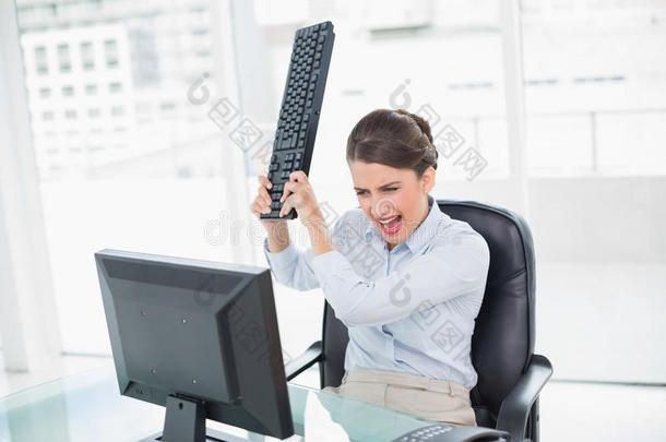 愤怒的时髦棕色头发的女商人把键盘扔在电脑上