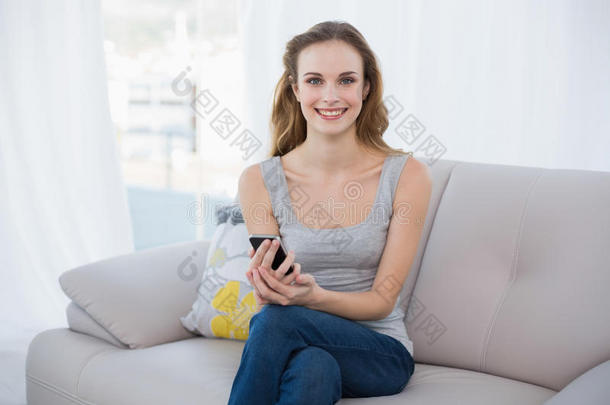 快乐的年轻<strong>女子坐在沙发上</strong>拿着智能手机
